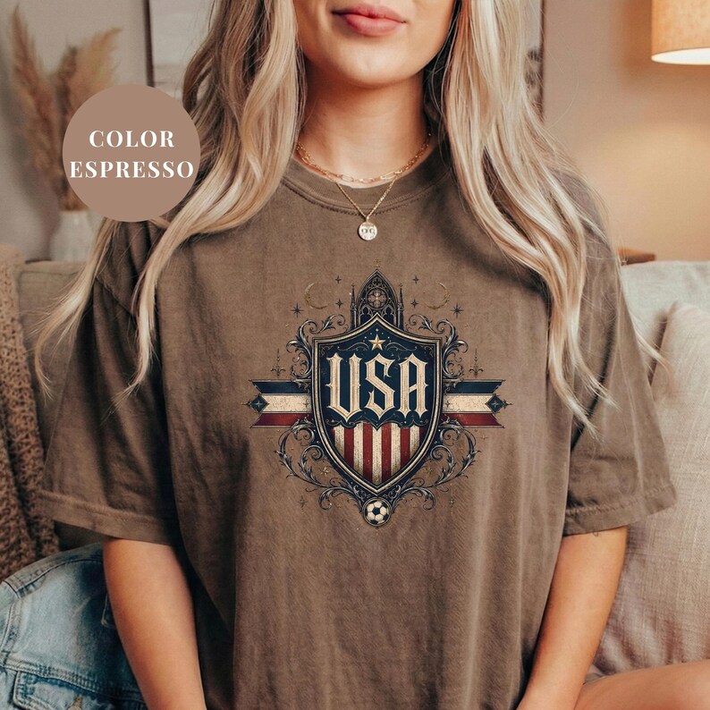 A woman wearing a brown t-shirt with a graphic design featuring the text "USA" and an American flag.