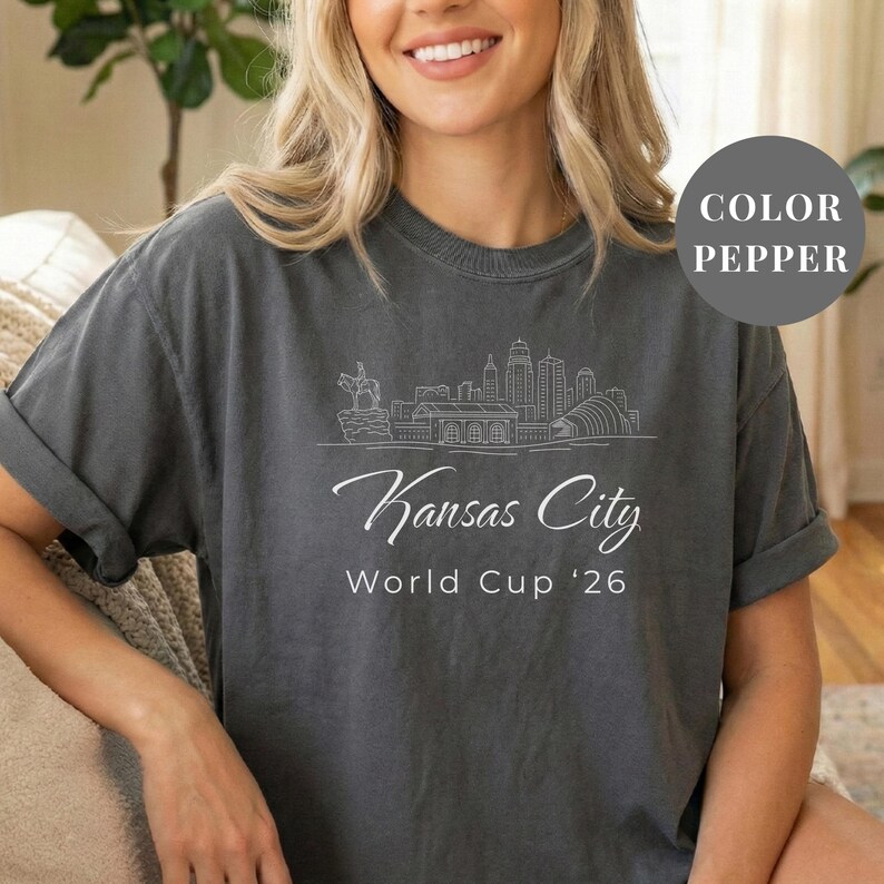Pepper Comfort Colors T-shirt featuring a minimalist white line art Kansas City skyline design, elegant Kansas City script lettering, and World Cup ’26 text, styled as a soccer travel souvenir shirt for Kansas City fans, football lovers, and 2026 World Cup city apparel.