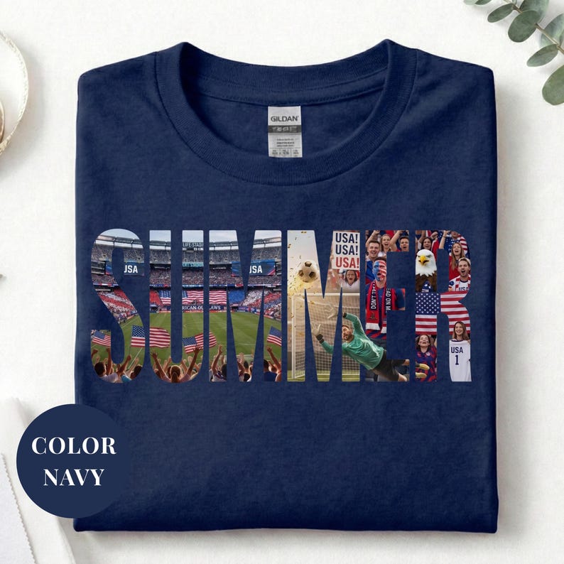 Navy Gildan t-shirt featuring a "SUMMER" photo collage graphic. The bold block letters are filled with USA soccer scenes, including a packed stadium, American flags, cheering fans, and a diving goalie. Patriotic sports apparel for World Cup 2026 supporters.