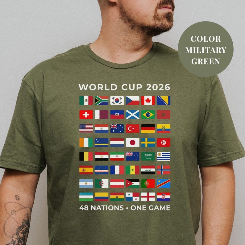 Green t-shirt featuring a comprehensive grid of 48 national flags for the World Cup 2026. The design includes bold "WORLD CUP 2026" text at the top and the slogan "48 NATIONS • ONE GAME" at the bottom. Premium international soccer fan apparel for the upcoming world tournament in North America.