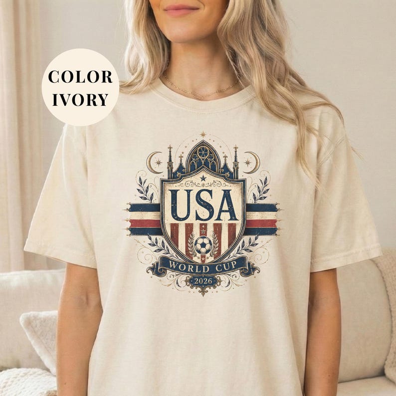 A woman wearing a white t-shirt with a graphic design featuring the text "USA WORLD CUP 2020" and a shield-like emblem with a flag and stars.