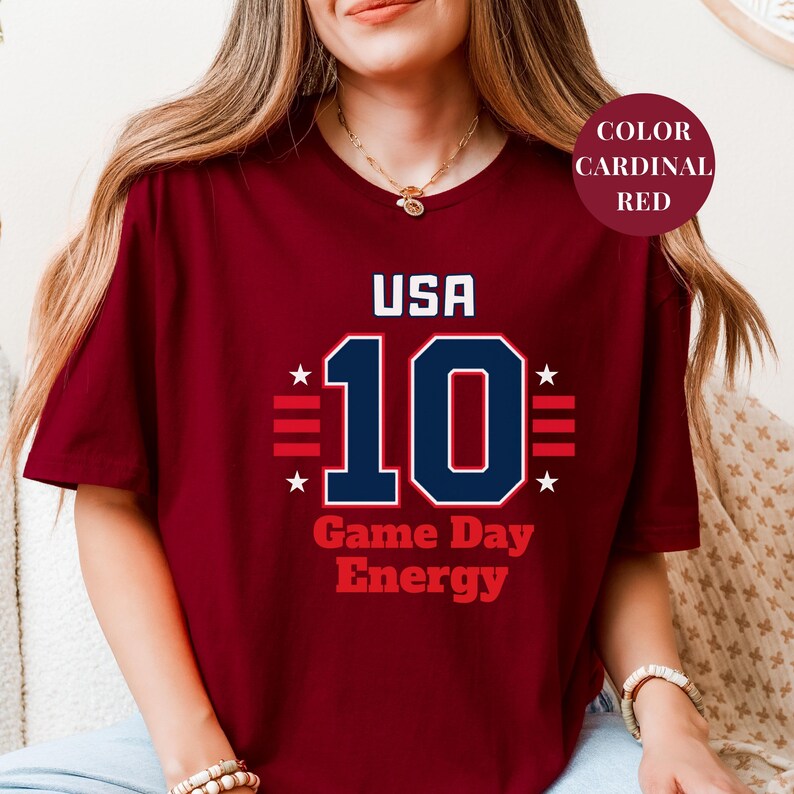 A woman wearing a maroon t-shirt with the text "USA 10 Game Day Energy" printed on it.