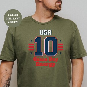 A man wearing a green t-shirt with a graphic design featuring the text "USA 10 Game Day Energy" and the number 10.