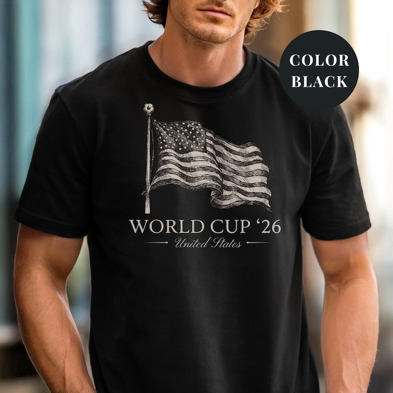Black Comfort Colors 1717 t-shirt featuring a vintage hand-drawn sketch of a waving American flag. Includes "WORLD CUP '26" and "United States" text, with a subtle soccer ball detail on the flagpole. High-quality patriotic soccer apparel for the 2026 world tournament fans.