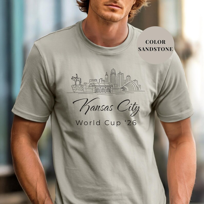 Sandstone Comfort Colors T-shirt featuring a minimalist black line art Kansas City skyline design, elegant Kansas City script lettering, and World Cup ’26 text, styled as a soccer travel souvenir shirt for Kansas City fans, football lovers, and 2026 World Cup city apparel.