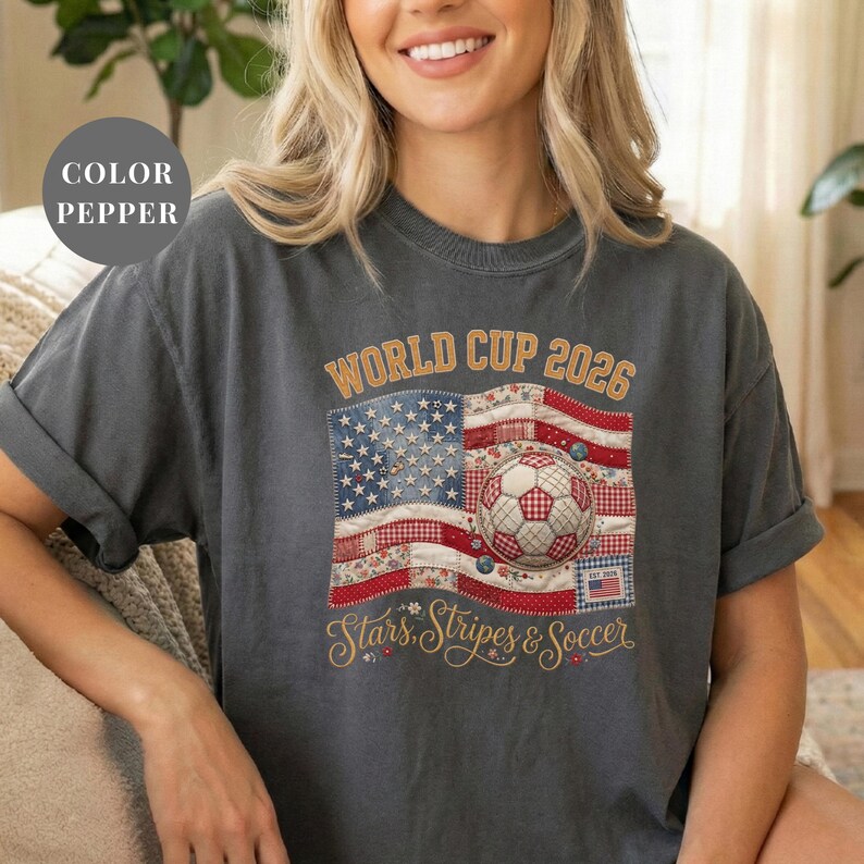 Pepper colored t-shirt featuring a vintage patchwork American flag design for World Cup 2026. The faux quilted graphic includes floral and gingham fabric textures, a stitched soccer ball, and "Stars, Stripes & Soccer" text. Unique patriotic sports apparel for women and USA soccer fans.