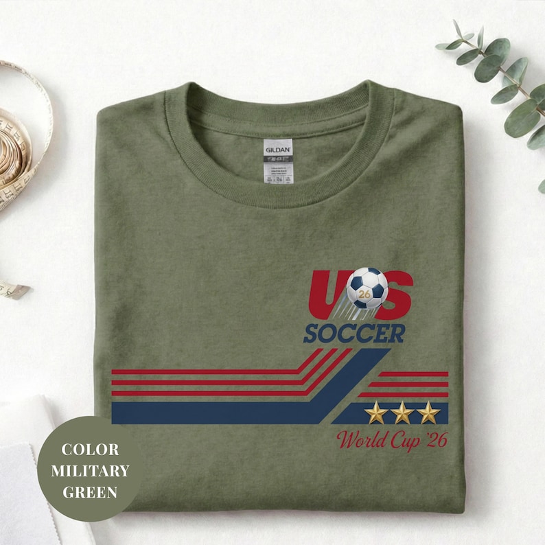 A green t-shirt with a graphic design featuring a soccer ball, stripes, and stars, along with the text "US SOCCER" and "World Cup 26".