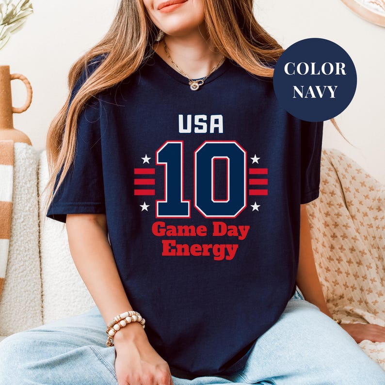 A woman wearing a navy blue t-shirt with the text "USA 10 Game Day Energy" printed on it.