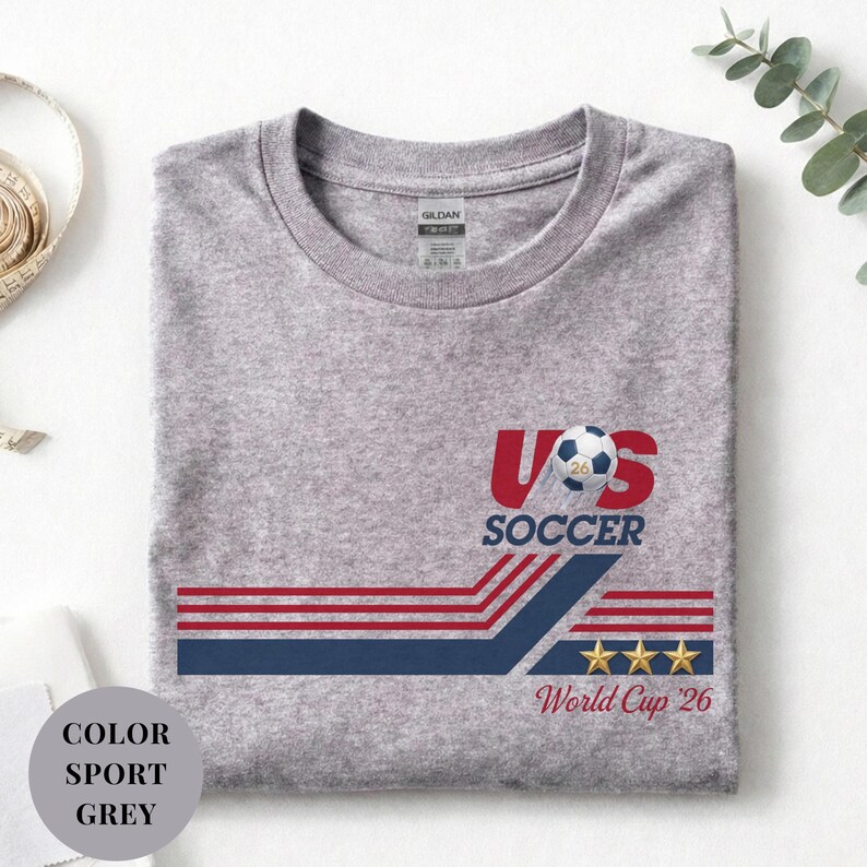 A gray t-shirt with a graphic design featuring a soccer ball, stripes, and stars, along with the text "US SOCCER World Cup 26" printed on it.