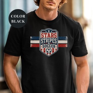 A man wearing a black t-shirt with a graphic design featuring the text "STARS STRIPS & SOCCER" and an American flag pattern.
