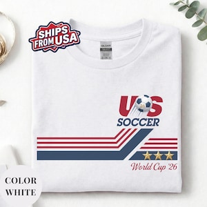 A white t-shirt with a graphic design featuring a soccer ball, stripes, and stars, along with text related to the US Soccer World Cup.
