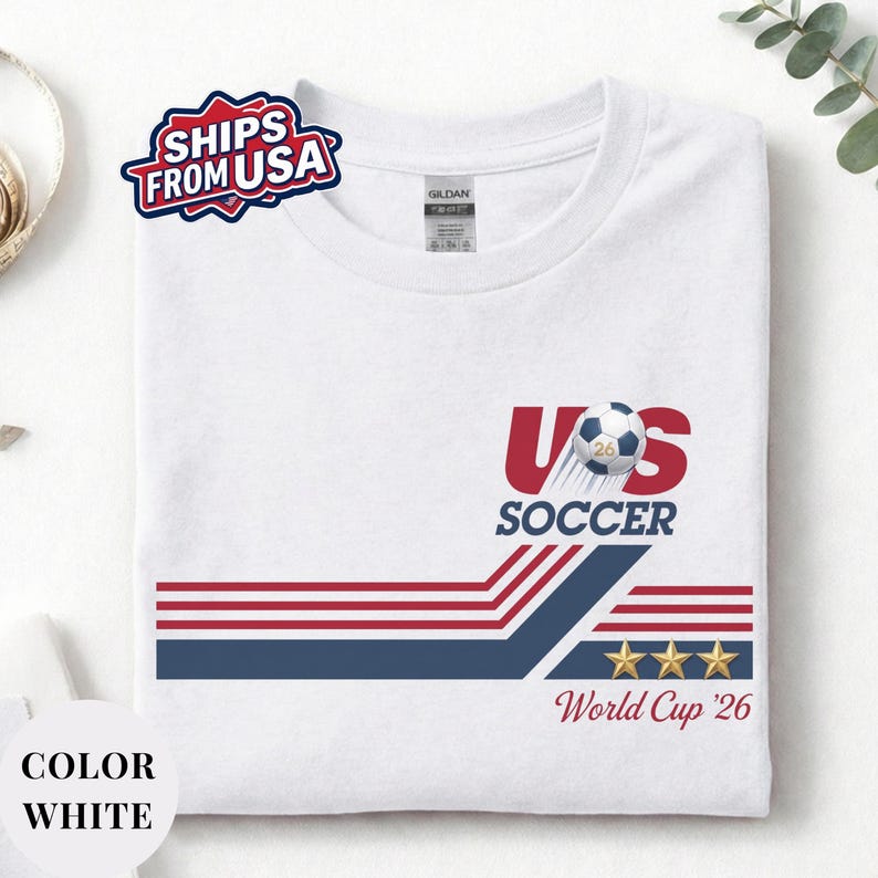 A white t-shirt with a graphic design featuring a soccer ball, stripes, and stars, along with text related to the US Soccer World Cup.