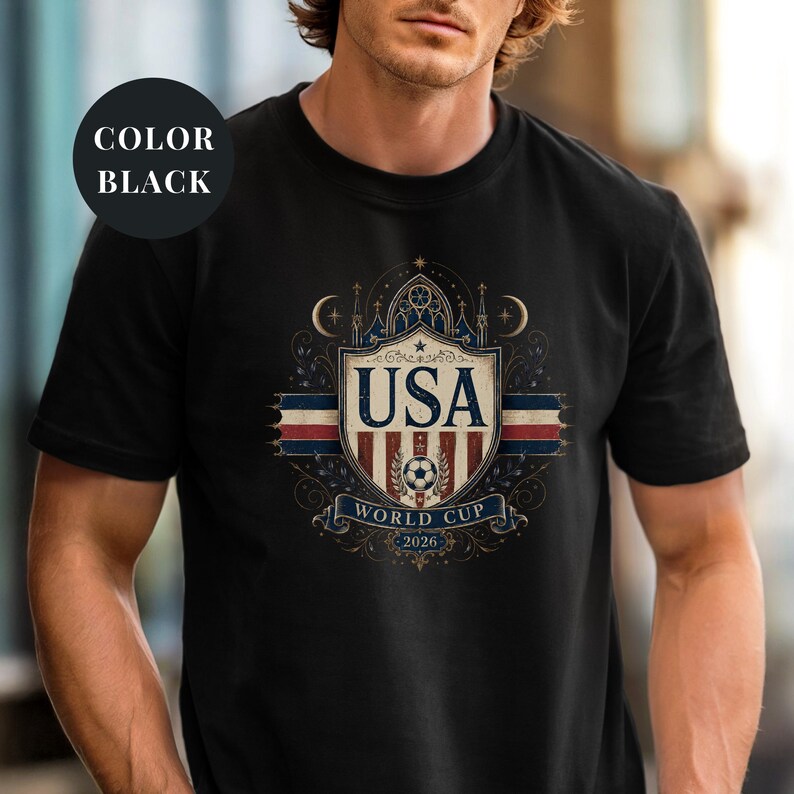 A man wearing a black t-shirt with a graphic design featuring the text "USA WORLD CUP 2026" and a shield-shaped emblem.