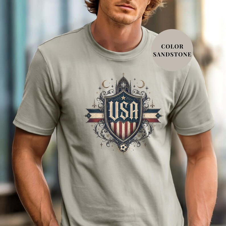 A man wearing a gray t-shirt with a graphic design featuring the text "USA" and a shield-like emblem with stars and a crescent moon.
