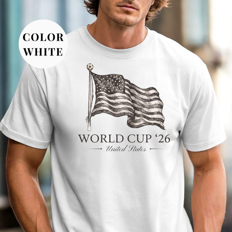 White Comfort Colors 1717 t-shirt featuring a vintage hand-drawn sketch of a waving American flag. Includes "WORLD CUP '26" and "United States" text, with a subtle soccer ball detail on the flagpole. High-quality patriotic soccer apparel for the 2026 world tournament fans.