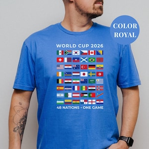 Royal blue t-shirt featuring a comprehensive grid of 48 national flags for the World Cup 2026. The design includes bold "WORLD CUP 2026" text at the top and the slogan "48 NATIONS • ONE GAME" at the bottom. Premium international soccer fan apparel for the upcoming world tournament in North America.