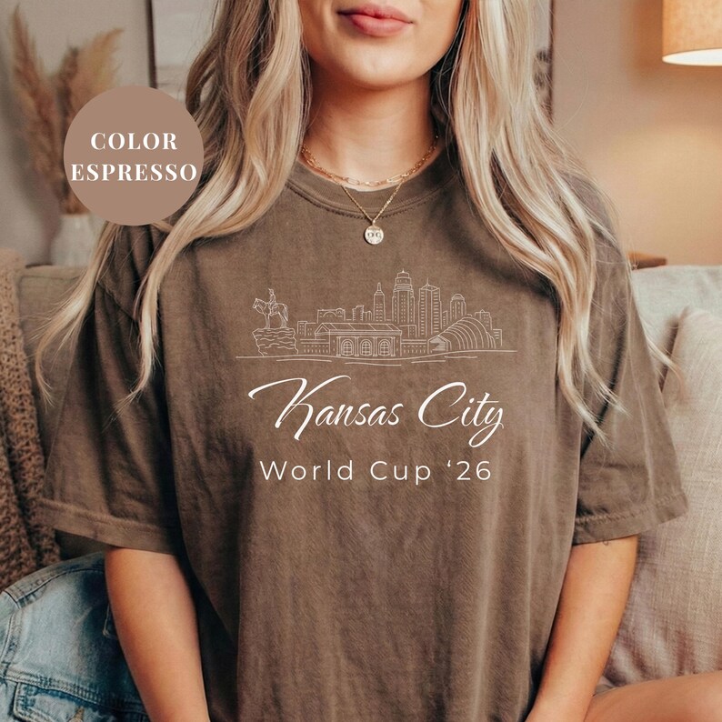 Espresso Comfort Colors T-shirt featuring a minimalist black line art Kansas City skyline design, elegant Kansas City script lettering, and World Cup ’26 text, styled as a soccer travel souvenir shirt for Kansas City fans, football lovers, and 2026 World Cup city apparel.