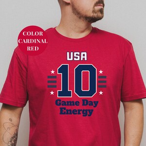 A man wearing a red t-shirt with the text "USA 10 Game Day Energy" printed on it.