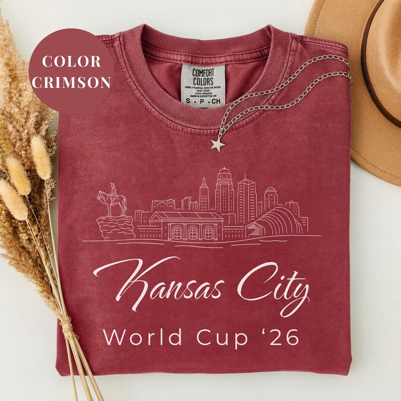 Crimson Comfort Colors T-shirt featuring a minimalist white line art Kansas City skyline design, elegant Kansas City script lettering, and World Cup ’26 text, styled as a soccer travel souvenir shirt for Kansas City fans, football lovers, and 2026 World Cup city apparel.