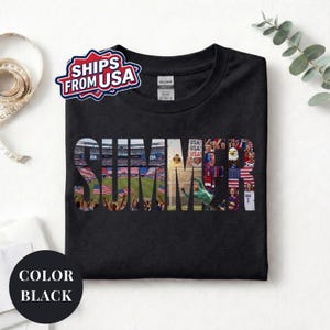 Black Gildan t-shirt featuring a "SUMMER" photo collage graphic. The bold block letters are filled with USA soccer scenes, including a packed stadium, American flags, cheering fans, and a diving goalie. Patriotic sports apparel for World Cup 2026 supporters.