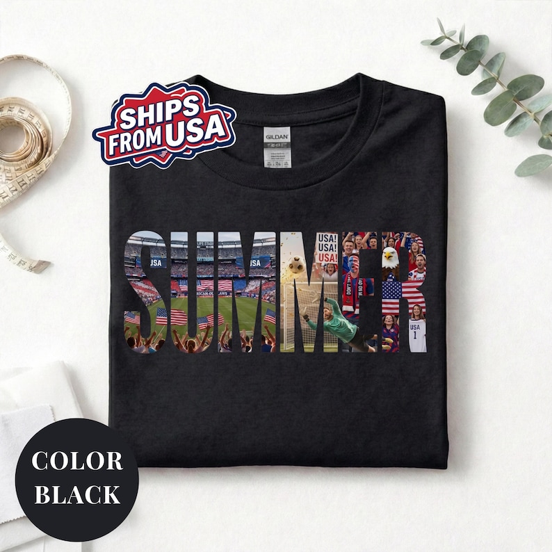 Black Gildan t-shirt featuring a "SUMMER" photo collage graphic. The bold block letters are filled with USA soccer scenes, including a packed stadium, American flags, cheering fans, and a diving goalie. Patriotic sports apparel for World Cup 2026 supporters.