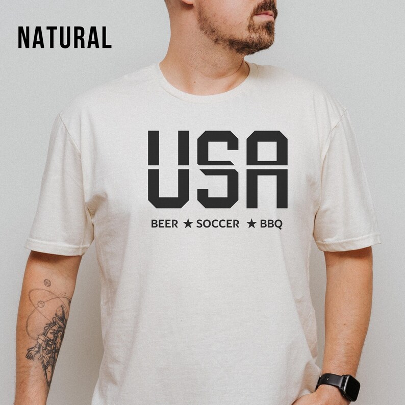 natural USA T-shirt for Soccer Fans featuring bold block letters and ‘Beer Soccer BBQ’ slogan, patriotic graphic tee for World Cup 2026 and game day wear.