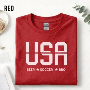 Red USA T-shirt for Soccer Fans featuring bold block letters and ‘Beer Soccer BBQ’ slogan, patriotic graphic tee for World Cup 2026 and game day wear.