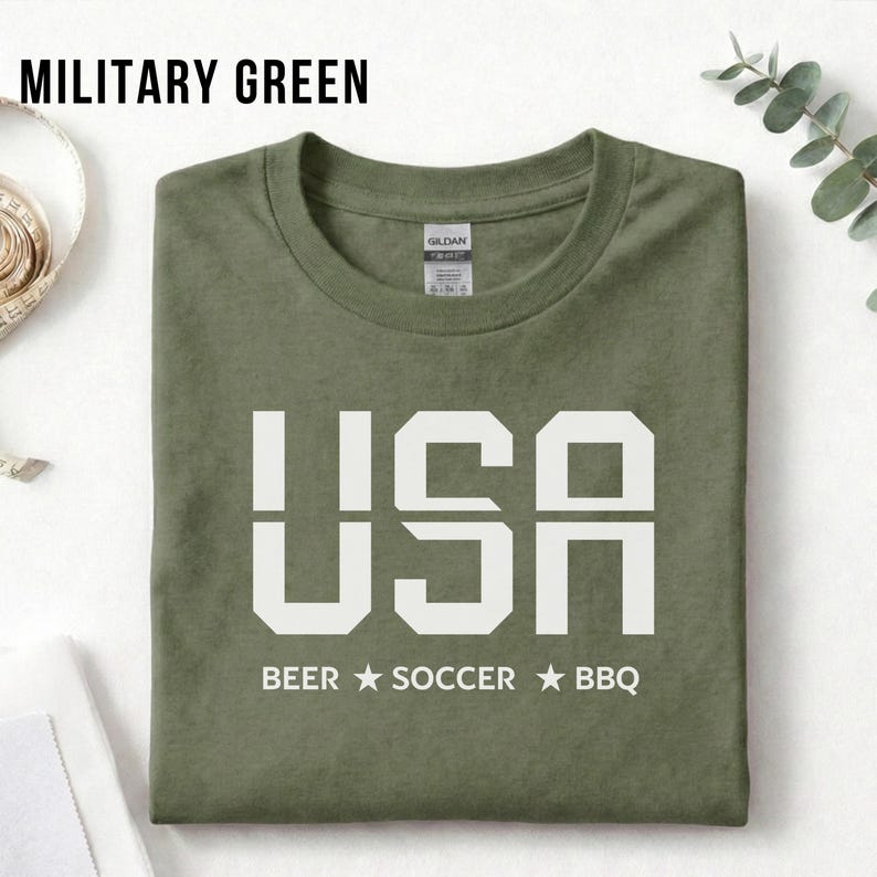 Military Green USA T-shirt for Soccer Fans featuring bold block letters and ‘Beer Soccer BBQ’ slogan, patriotic graphic tee for World Cup 2026 and game day wear.