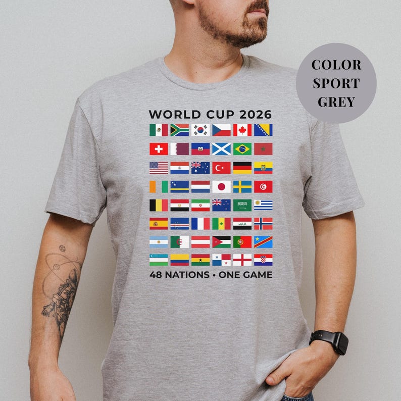 Grey t-shirt featuring a comprehensive grid of 48 national flags for the World Cup 2026. The design includes bold "WORLD CUP 2026" text at the top and the slogan "48 NATIONS • ONE GAME" at the bottom. Premium international soccer fan apparel for the upcoming world tournament in North America.