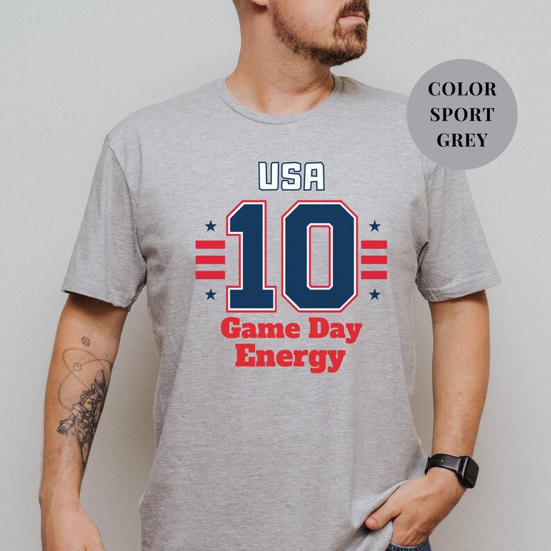 A man wearing a grey t-shirt with a graphic design featuring the text "USA 10 Game Day Energy" and the number 10.