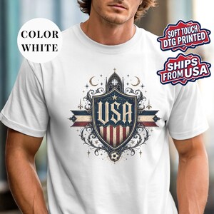 A man wearing a white t-shirt with a graphic design featuring a shield with the word "USA" printed on it.