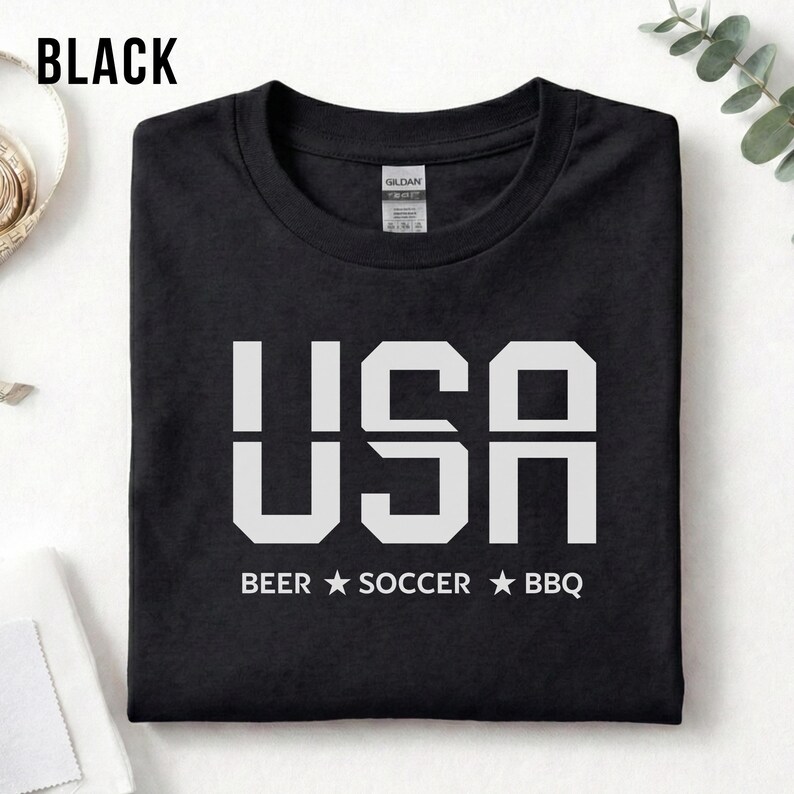 Black USA T-shirt for Soccer Fans featuring bold block letters and ‘Beer Soccer BBQ’ slogan, patriotic graphic tee for World Cup 2026 and game day wear.