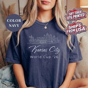 Navy Comfort Colors T-shirt featuring a minimalist black line art Kansas City skyline design, elegant Kansas City script lettering, and World Cup ’26 text, styled as a soccer travel souvenir shirt for Kansas City fans, football lovers, and 2026 World Cup city apparel.