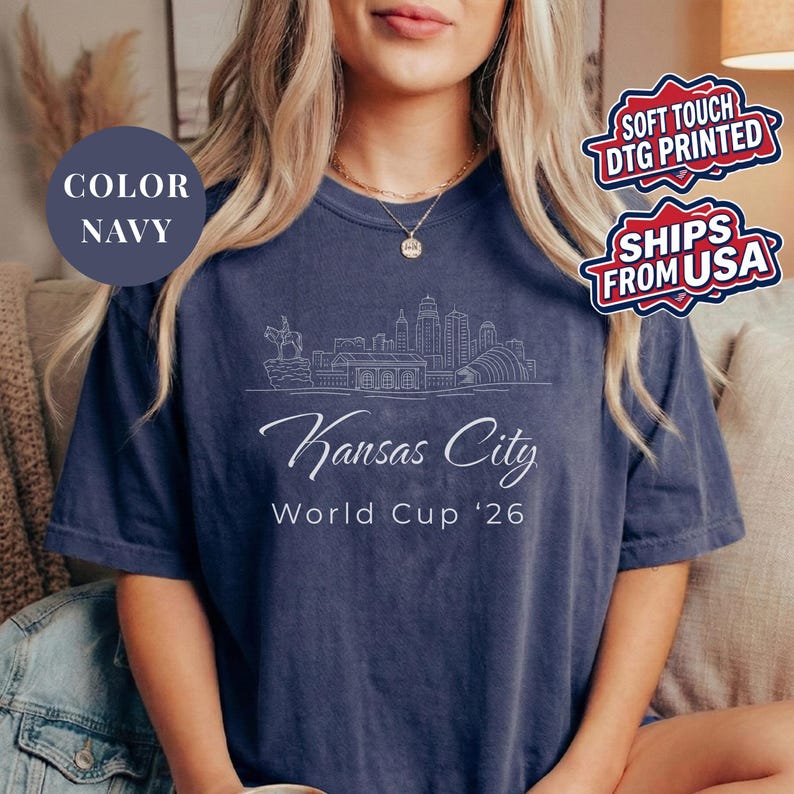 Navy Comfort Colors T-shirt featuring a minimalist black line art Kansas City skyline design, elegant Kansas City script lettering, and World Cup ’26 text, styled as a soccer travel souvenir shirt for Kansas City fans, football lovers, and 2026 World Cup city apparel.