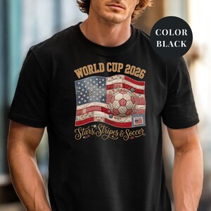 Black colored t-shirt featuring a vintage patchwork American flag design for World Cup 2026. The faux quilted graphic includes floral and gingham fabric textures, a stitched soccer ball, and "Stars, Stripes & Soccer" text. Unique patriotic sports apparel for women and USA soccer fans.