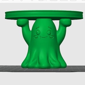Pu&ograve; includere: Un modello 3D verde brillante di un piccolo supporto con una figura centrale a forma di fantasma con le braccia sollevate che sostengono un piano circolare piatto. Il fantasma ha un volto sorridente con grandi occhi e guance rosate, reso digitalmente.