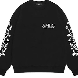 Pode incluir: Camisola preta de gola redonda com desenhos brancos semelhantes a ossos nas mangas. A palavra "AMIRI" está impressa em branco no peito, com "HOLLYWOOD.CA" abaixo. Estilo casual.