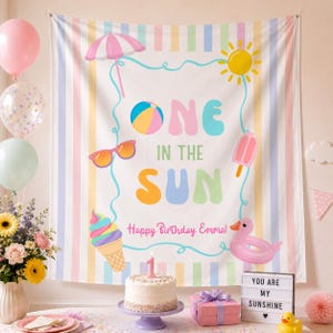 Może przedstawiać: Prostokątne tło z tkaniny w pastelowe pionowe paski z białym panelem pośrodku z napisem ONE IN THE SUN oraz Happy Birthday Emma. Ilustracje przedstawiają parasol plażowy, słońce, piłkę plażową, okulary przeciwsłoneczne, loda na patyku, rożek lodowy i różowe koło do pływania w kształcie kaczki.