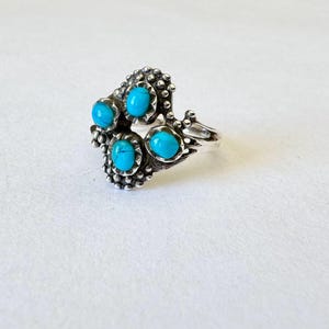 May include: A silver ring featuring five turquoise-colored stones. The ring has a detailed, textured design around the stones and band. The turquoise stones are oval-shaped and set in a cluster pattern.