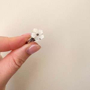 May include: A silver ring featuring a white flower design. The flower has a small silver centre.