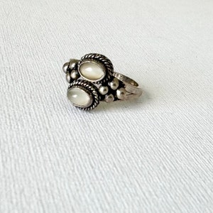 May include: A silver ring featuring two oval white stones set in a beaded design.