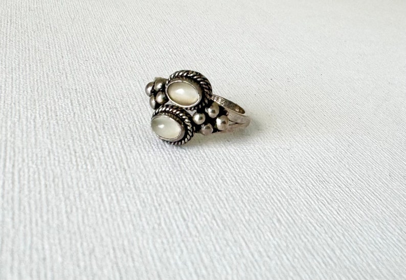 May include: A silver ring featuring two oval white stones set in a beaded design.