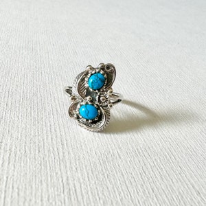 May include: A silver ring with two turquoise stones set in a swirling design.