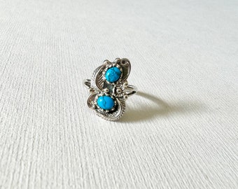 May include: A silver ring featuring two turquoise stones set in a swirling design.