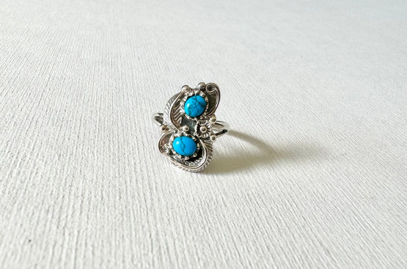 May include: A silver ring with two turquoise stones set in a swirling design.