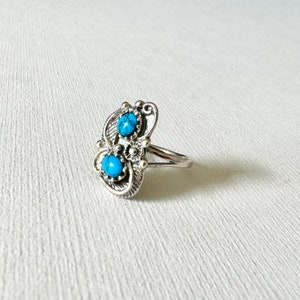 May include: A silver ring with two turquoise stones set in a floral design.
