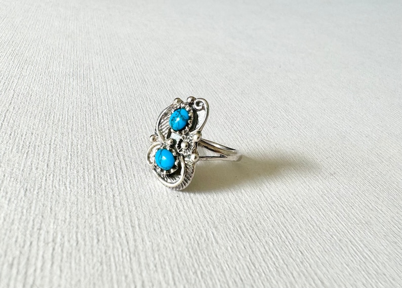 May include: A silver ring with two turquoise stones set in a floral design.