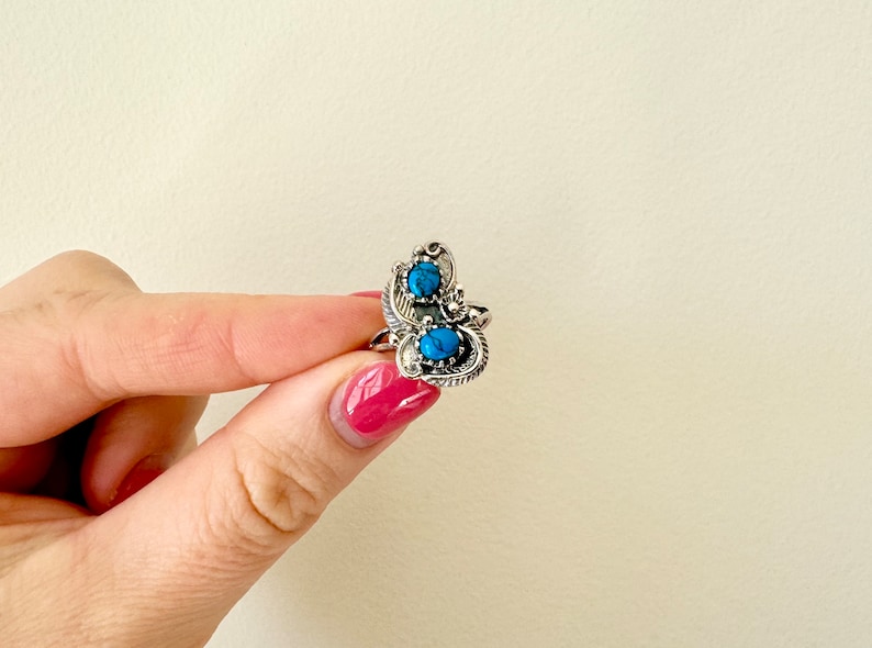 May include: A silver ring with two turquoise stones set in a decorative design.