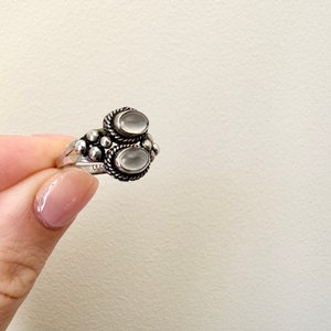 May include: A silver ring featuring two oval white stones set in a beaded design.
