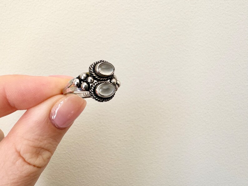 May include: A silver ring featuring two oval white stones set in a beaded design.